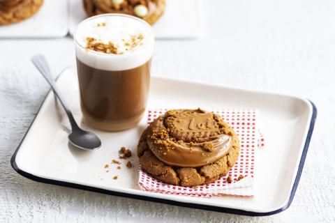bandeja con un chocolate caliente y nata en un vaso y cookie cubierta de crema de untar y una galleta lotus biscoff