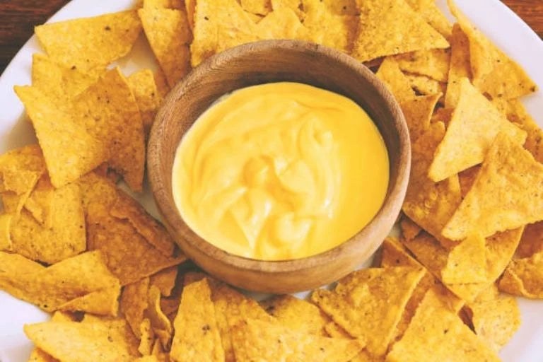 Queso fundido en tazón de madera sobre una cama de totopos dorados.