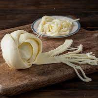 queso de oaxaca en bola mostrando sus hilos sobre una tabla de madera y con un lato con mas hilos de queso