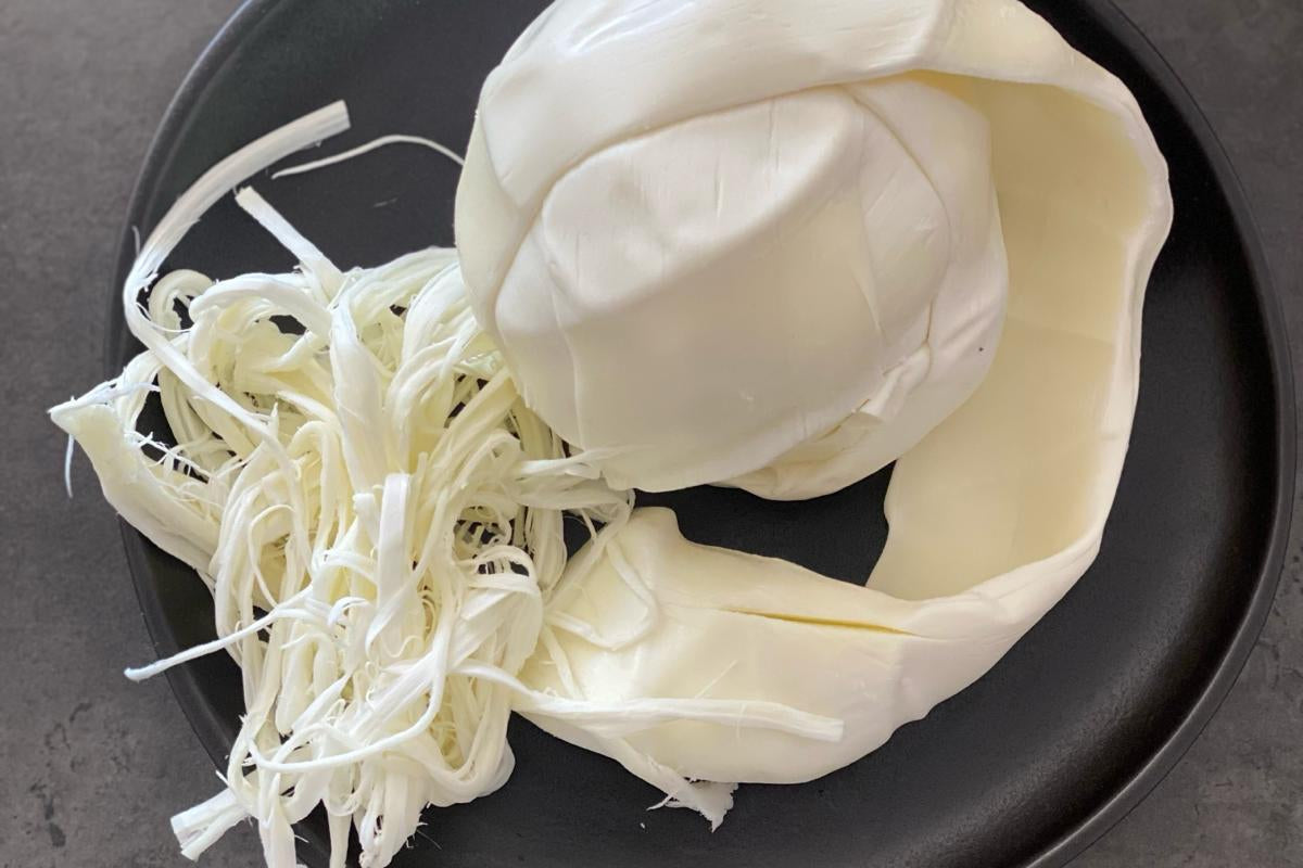 Sobre un plato negro, bola de queso oaxaqueño en el que se aprecia una parte deshilachada característica de este producto