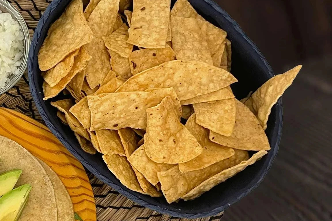 Totopos en un recipiente negro con guacamole y cebolla como acompañamiento.