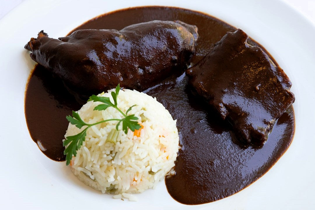 Plato con pollo y cerdo bañados en mole negro, acompañado de un timbal de arroz decorado con perejil fresco.