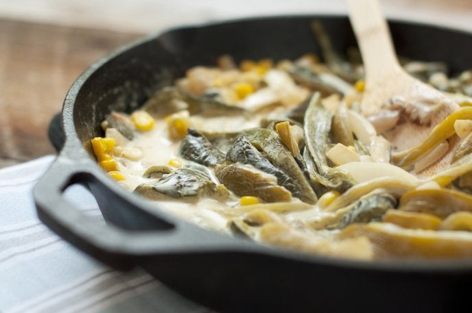 Rajas de chile poblano cocinadas con crema, elote y cebolla en un sartén de hierro fundido.