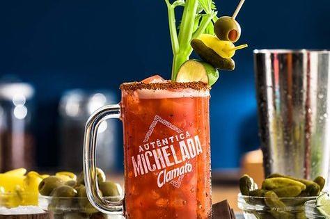 Michelada preparada con Clamato, servida en una jarra escarchada, decorada con apio, aceitunas y chile en polvo para un toque picante.