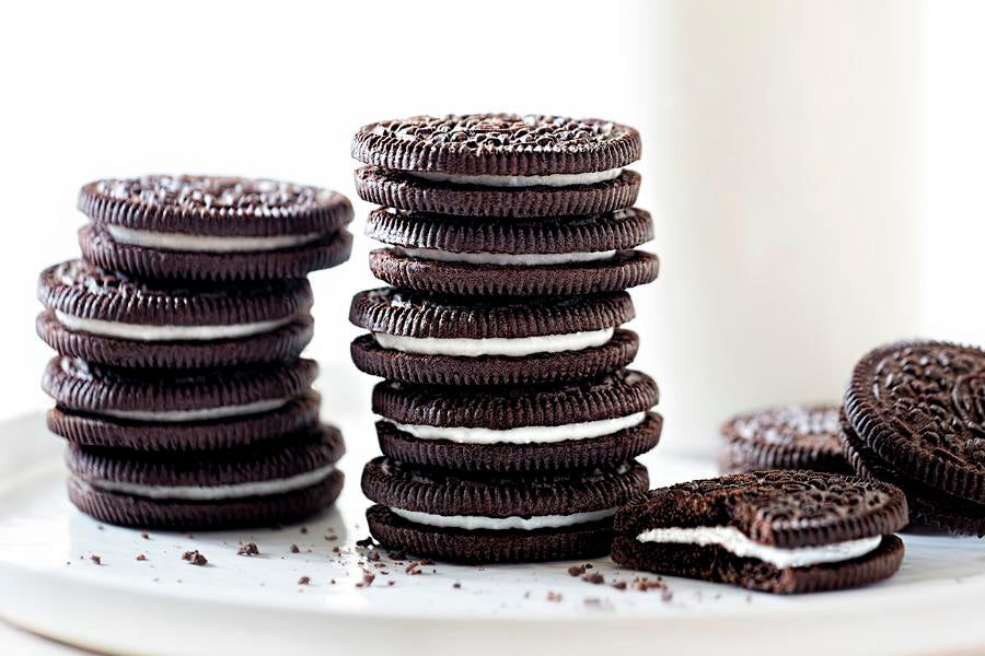 sobre un fondo y en un plato blanco dos grupos de galletas oreo apiladas y en primer termino una que aparece mordisqueada