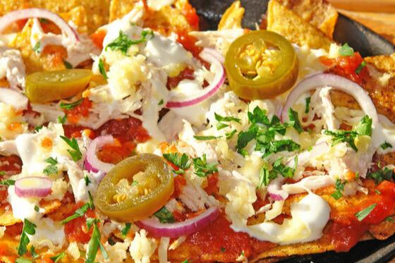 Plato de nachos con jalapeños, cebolla morada, queso y crema, adornados con cilantro fresco.