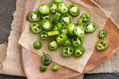 Rodajas de jalapeño fresco dispuestas en una tabla de madera rústica, listas para cocinar o decorar platillos.