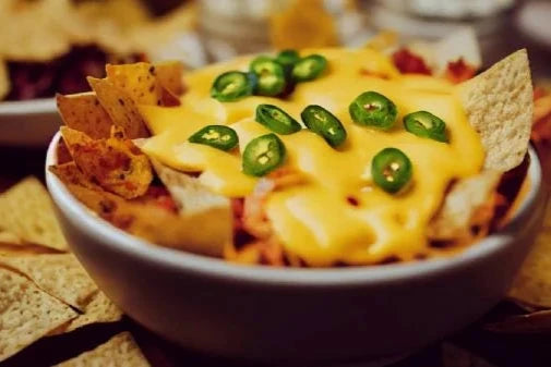 Tazón de nachos con queso cheddar derretido y rodajas de jalapeño picante.