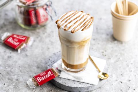 vaso de cafe latte con adorno de crema biscoff, varias galletas envasadas indic¡vidualmente con la marca sobre plato y encimera cerámicos