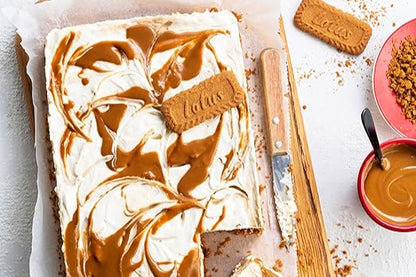 sobre una tabla de madera tarta y migas de galletas biscoff un bol de crema, cuchillo, una galleta y un plato con migas de galleta