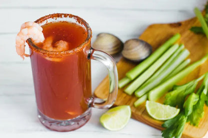 Michelada de camarón con Clamato, acompañada de apio, limón y almejas frescas, servida en una jarra escarchada con chile.