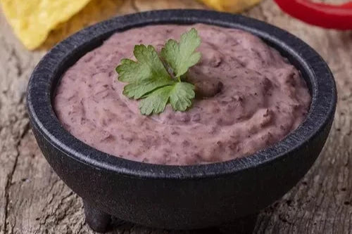 Molcajete con frijoles negros refritos, decorados con perejil fresco, listo para disfrutar con totopos crujientes.