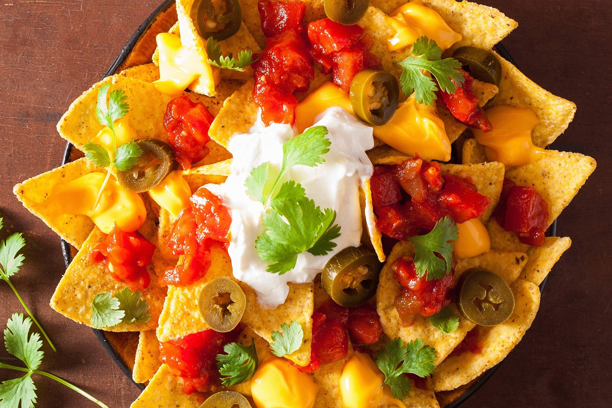 Nachos tradicionales con queso derretido, jalapeños en rodajas, salsa roja y crema, decorados con cilantro fresco