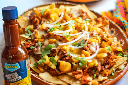 Nachos estilo al pastor con piña, cebolla y cilantro, acompañados de marinador "La Anita" al lado del platillo.