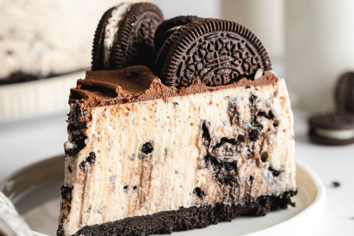 trozo de pastel cheesecake con galletas oreo en un plato blanco con trocitos de galleta en la base y galletas incrustadas en lo alto