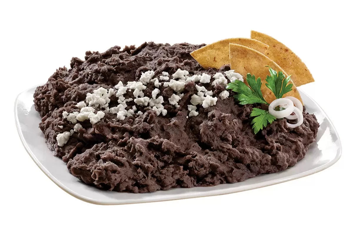 Plato de frijoles negros refritos decorado con queso fresco, totopos y ramitas de perejil, ideal como guarnición o entrada.