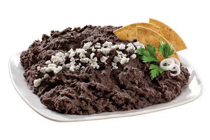 Plato de frijoles negros refritos decorado con queso fresco, totopos y ramitas de perejil, ideal como guarnición o entrada.