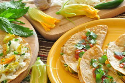 Quesadilla rellena de flor de calabaza y queso fundido en una tortilla de maíz, acompañada de flores frescas como decoración.