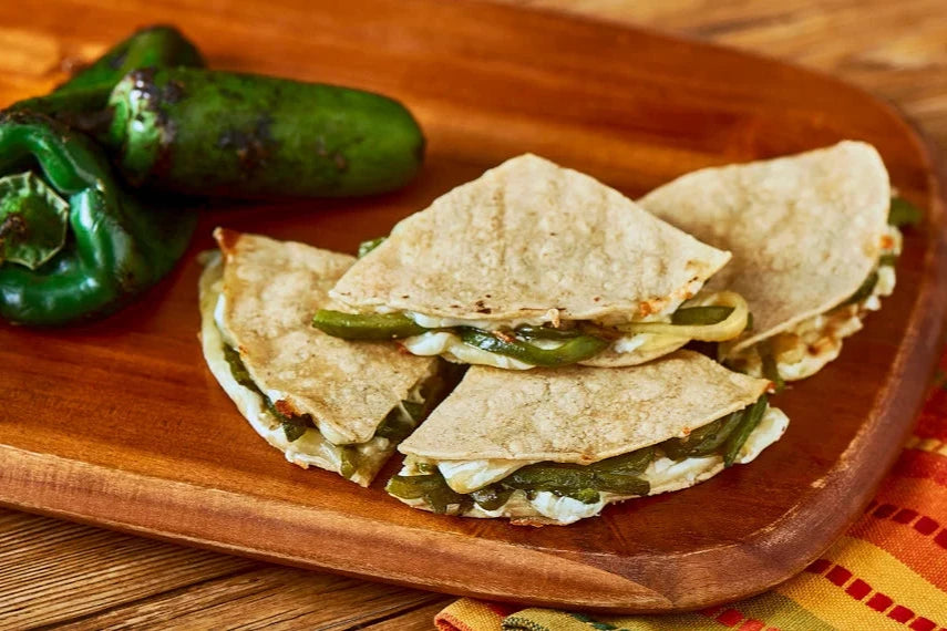 Quesadillas rellenas de rajas de chile poblano y queso, acompañadas de chiles frescos en una tabla de madera.
