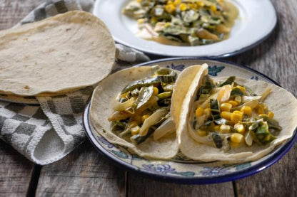 Tacos servidos en tortillas de maíz, rellenos de rajas de chile poblano, elote y crema.