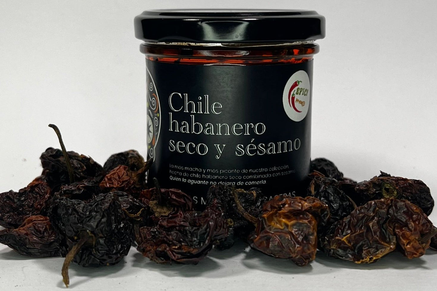 Frasco de salsa de chile habanero seco con sésamo, rodeado de chiles habaneros deshidratados en un fondo blanco