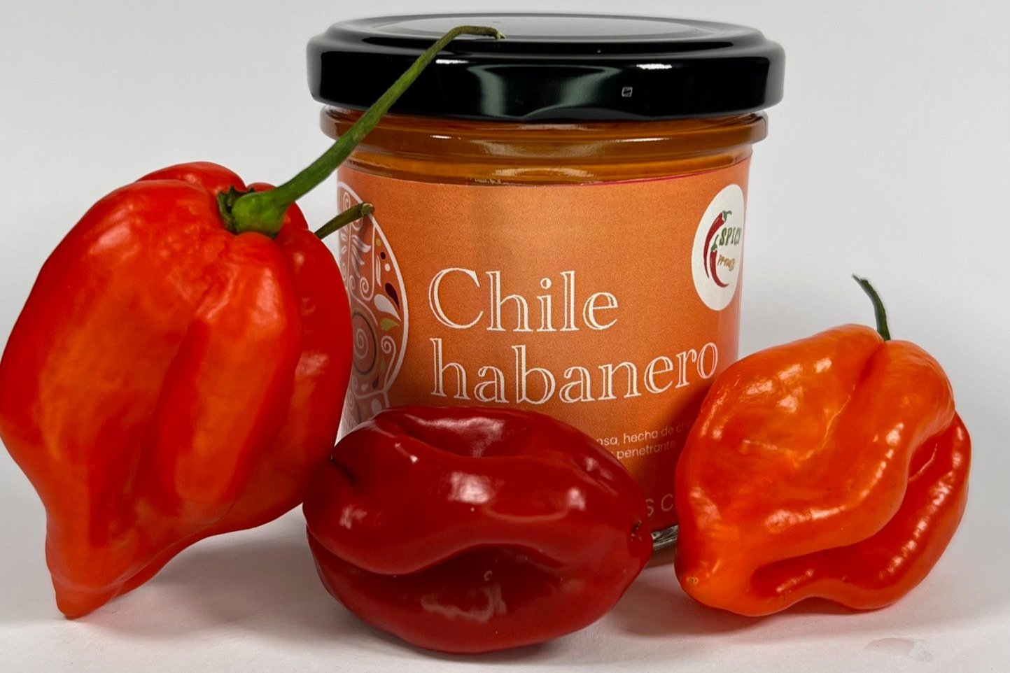 Frasco de salsa artesanal de chile habanero con chiles frescos rojos como decoración en un fondo claro.