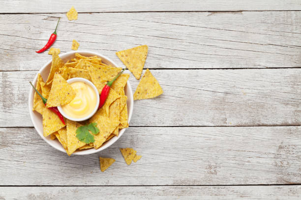 Cuenco con totopos, nachos y un pequeño cuenco con salsa de queso sobre estos. Fondo de madera blanca