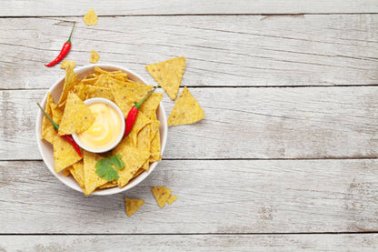 Cuenco con totopos, nachos y un pequeño cuenco con salsa de queso sobre estos. Fondo de madera blanca