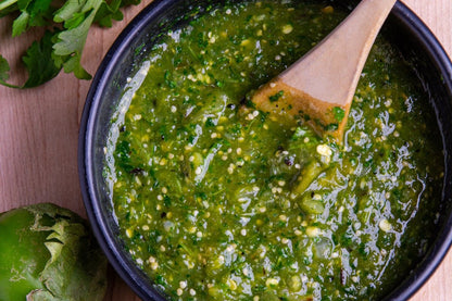 Salsa verde espesa en tazón con tomatillos y cilantro fresco, acompañada de limón para un toque cítrico