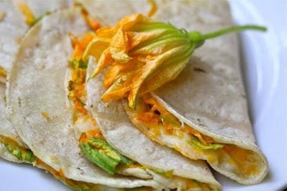 Tacos de flor de calabaza servidos en tortillas calientes, decorados con cilantro fresco, ideales para una comida tradicional.