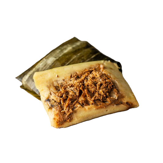 Tamal con salsa roja y carne deshebrada, cocido al vapor en hoja de plátano.