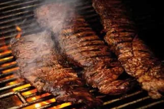 Tres cortes de carne asándose en parrilla con llamas y humo, ideal para barbacoa.