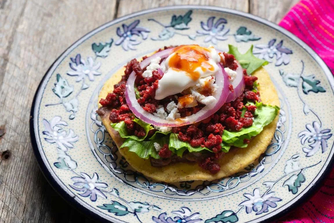 Tostada casera con huevo tierno, frijoles y salsa de chile verde sobre un plato colorido.