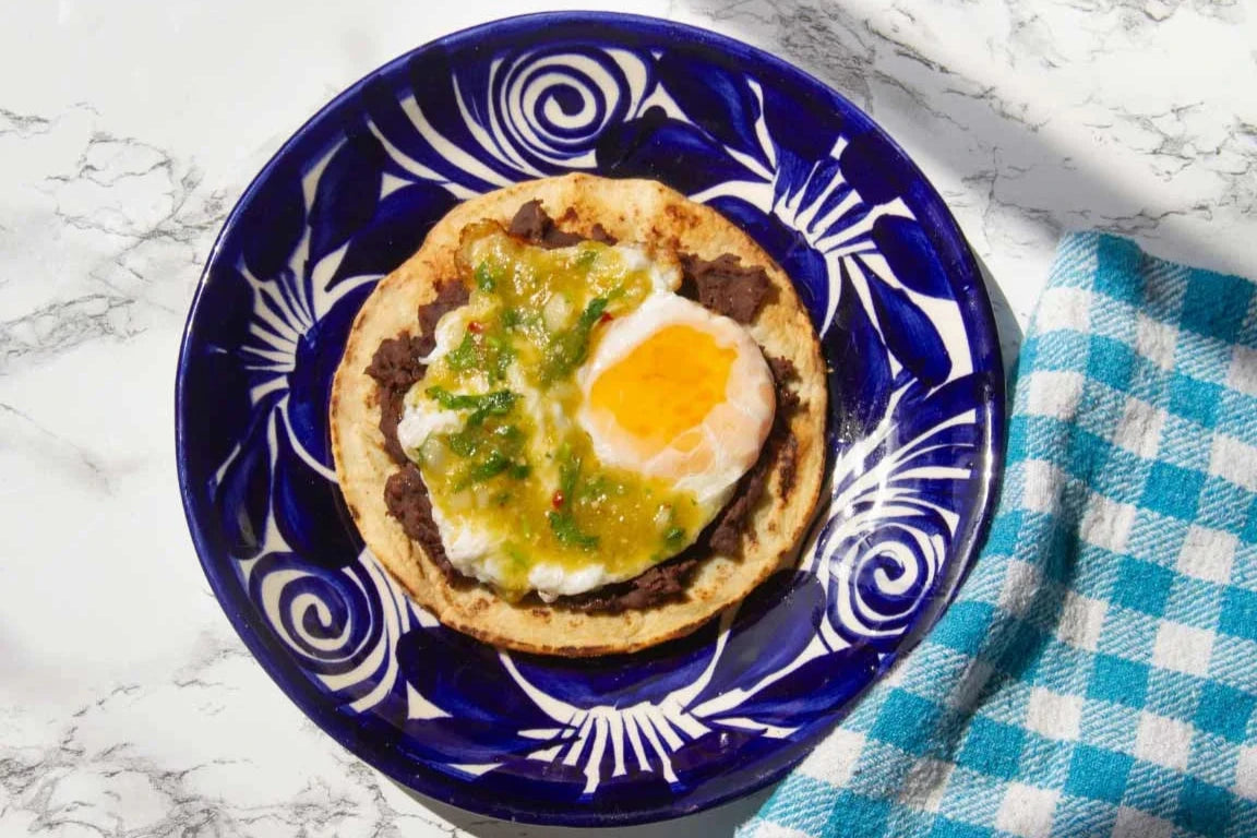 Tostada tradicional mexicana con huevo, frijoles refritos y salsa verde casera, ideal para el desayuno.